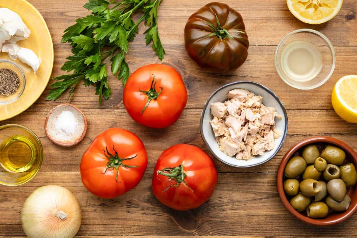 ingredients for stuffed tomatoes with tuna including tomatoes, tuna, olive oil, olives, onion, salt, pepper, garlic, parsley and lemon juice.