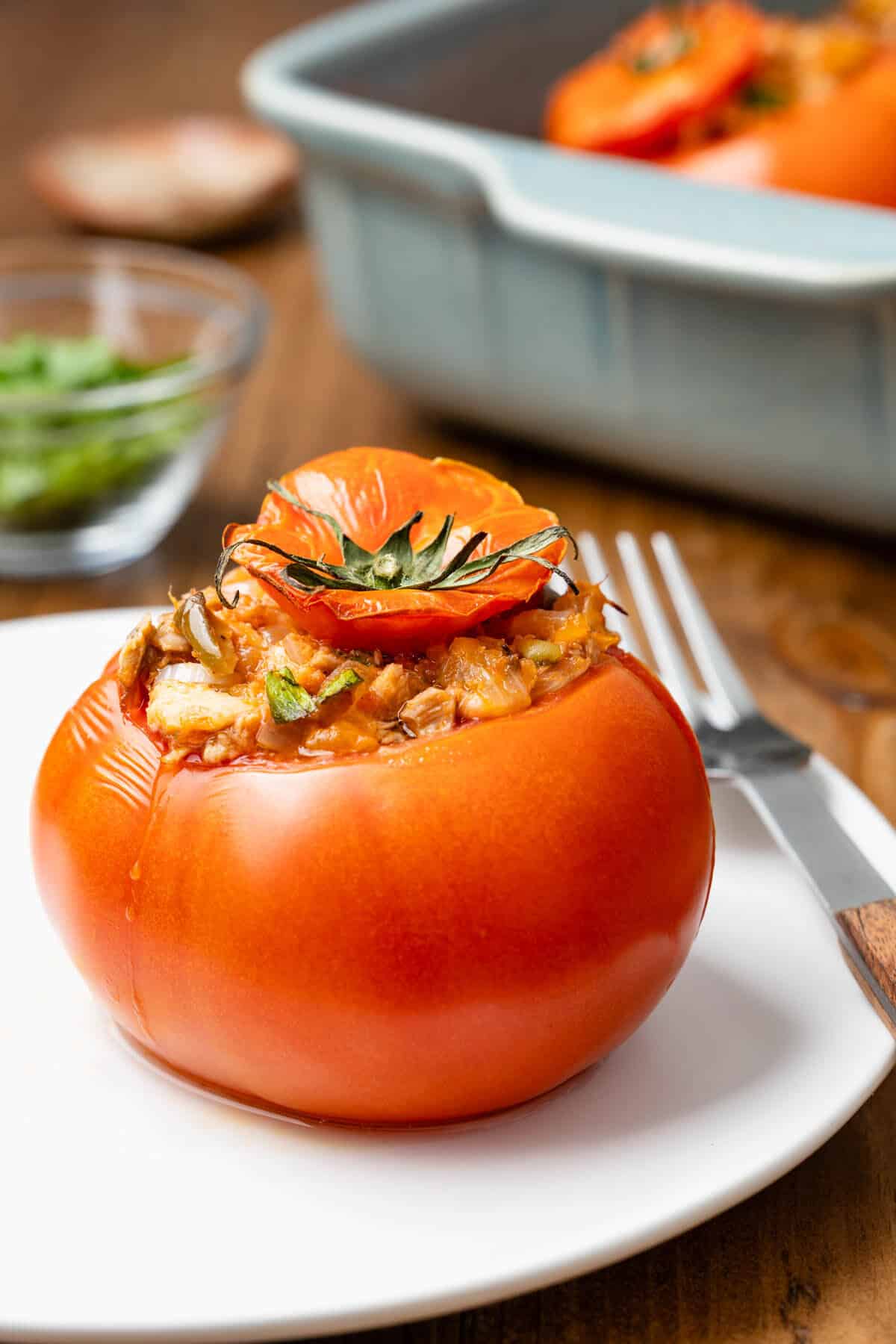 a baked stuffed tomato with tuna on a white plate with a fork.