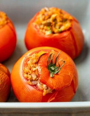 close up of a baked stuffed tomato with tuna in a baking dish with others in the background.