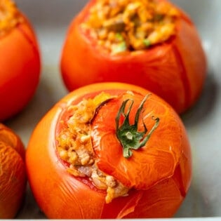 close up of a baked stuffed tomato with tuna in a baking dish with others in the background.