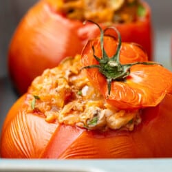 close up of a baked stuffed tomato with tuna in a baking dish with another one in the background.