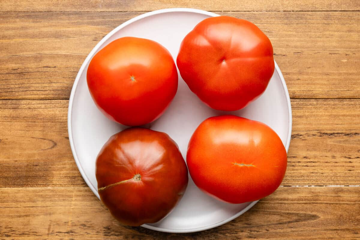 four whole tomatoes on a white plate.