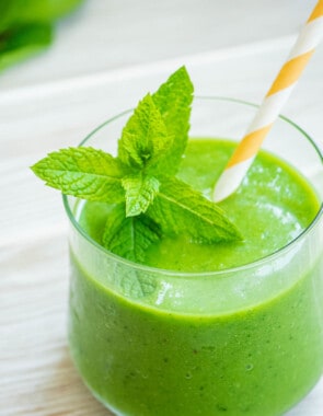 a vegan green smoothie in a glass with fresh mint and a yellow and white straw.