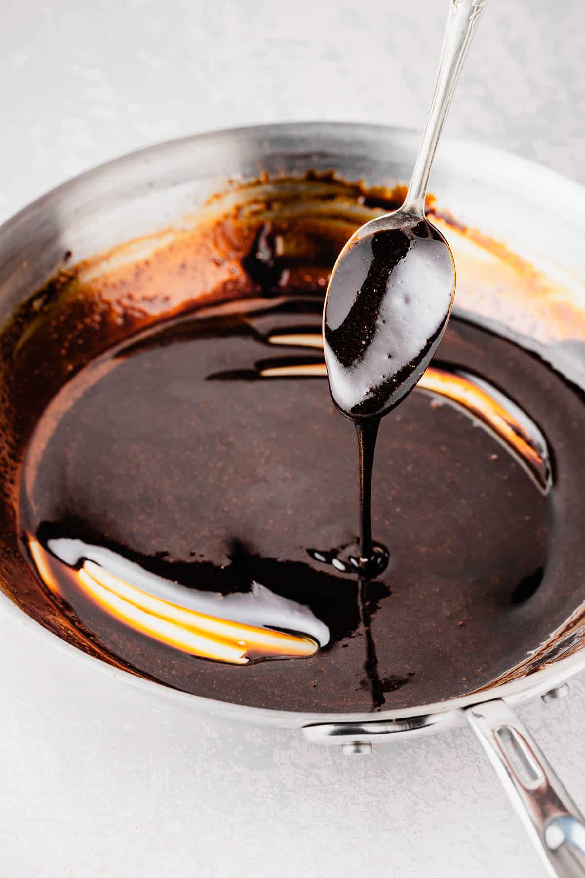 balsamic glaze being drizzled from a spoon into a skillet.