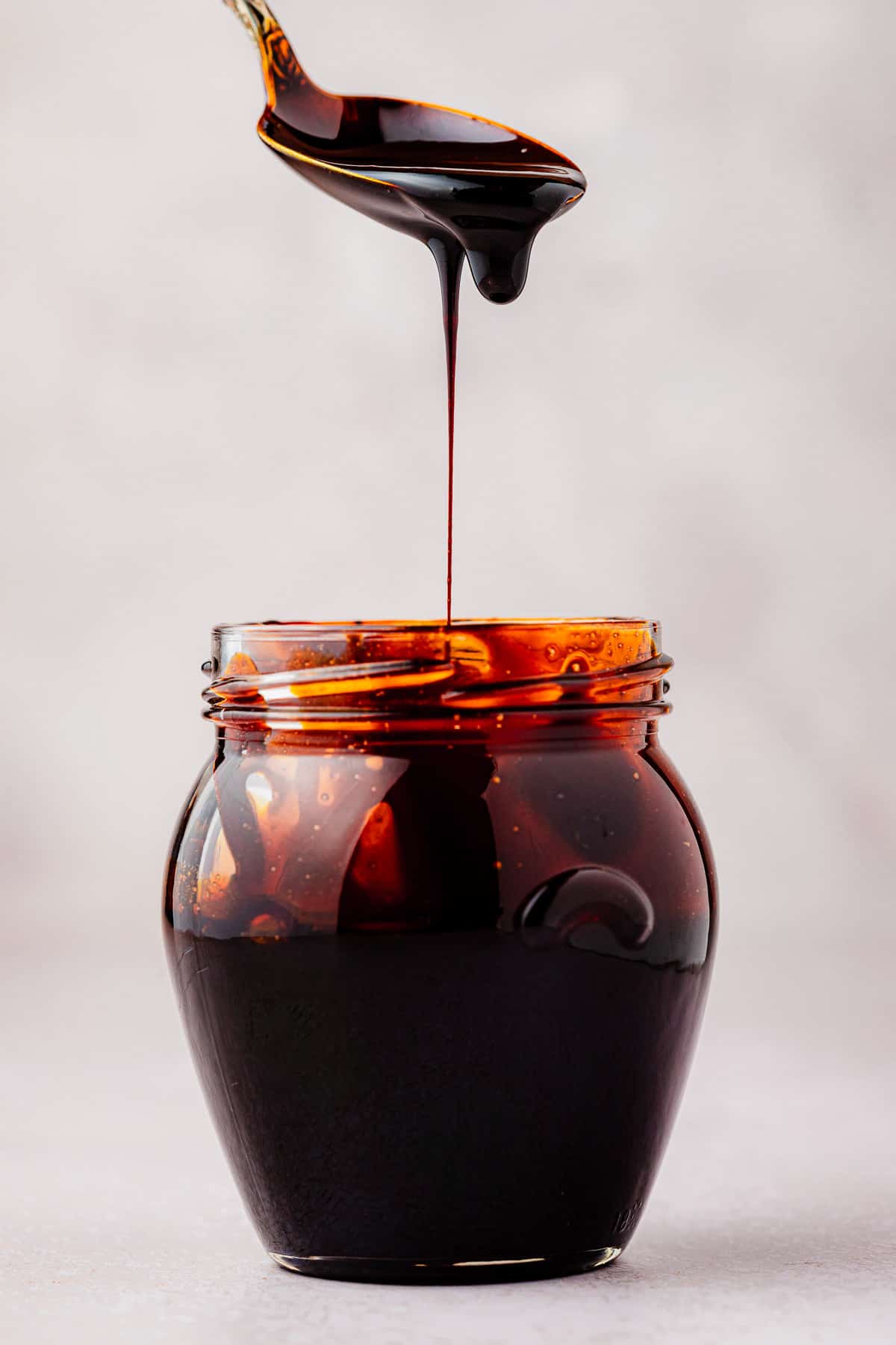 balsamic glaze being drizzled from a spoon into a jar.