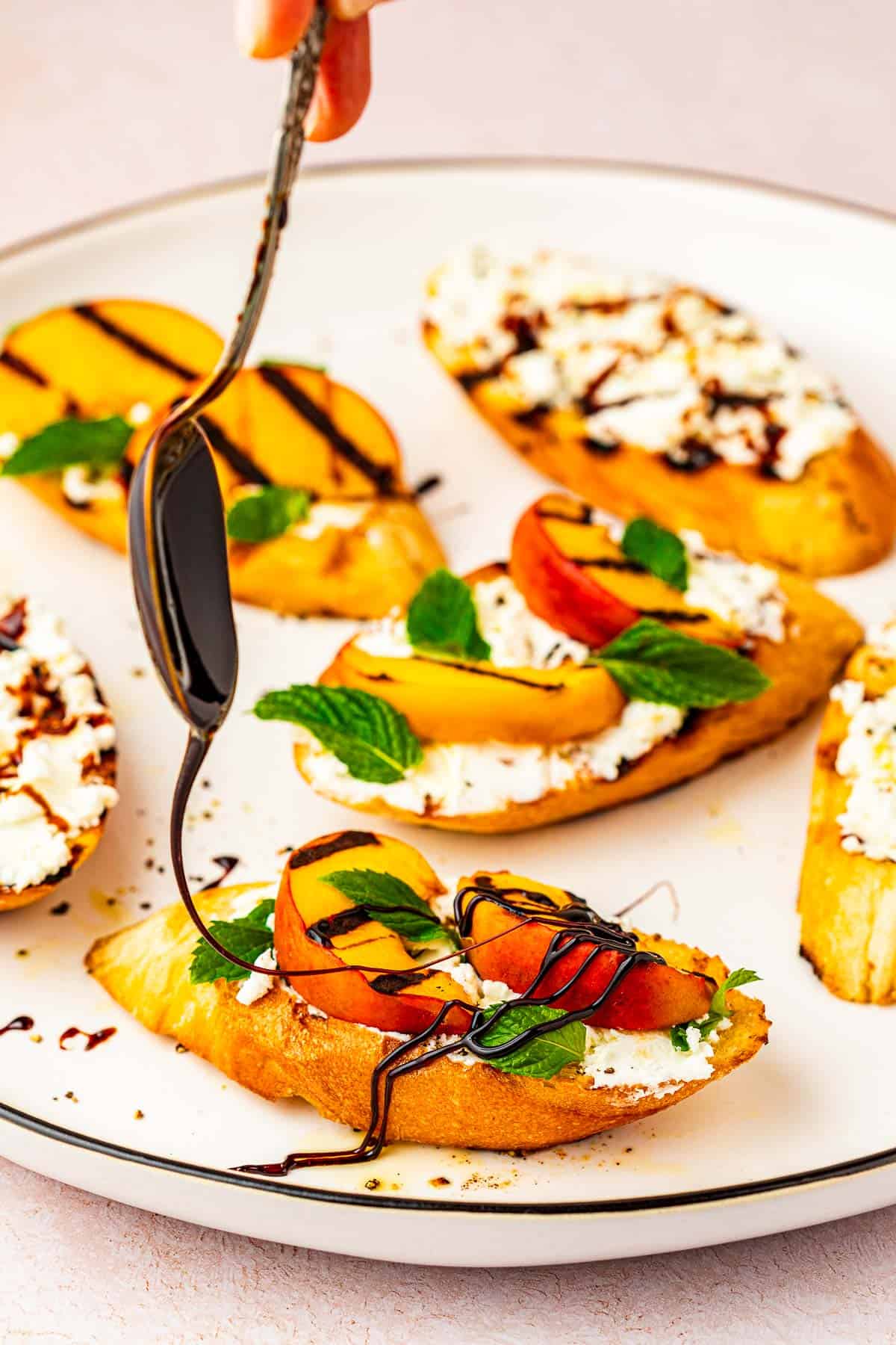 balsamic glaze being drizzled on a piece of a peach bruschetta appetizer.