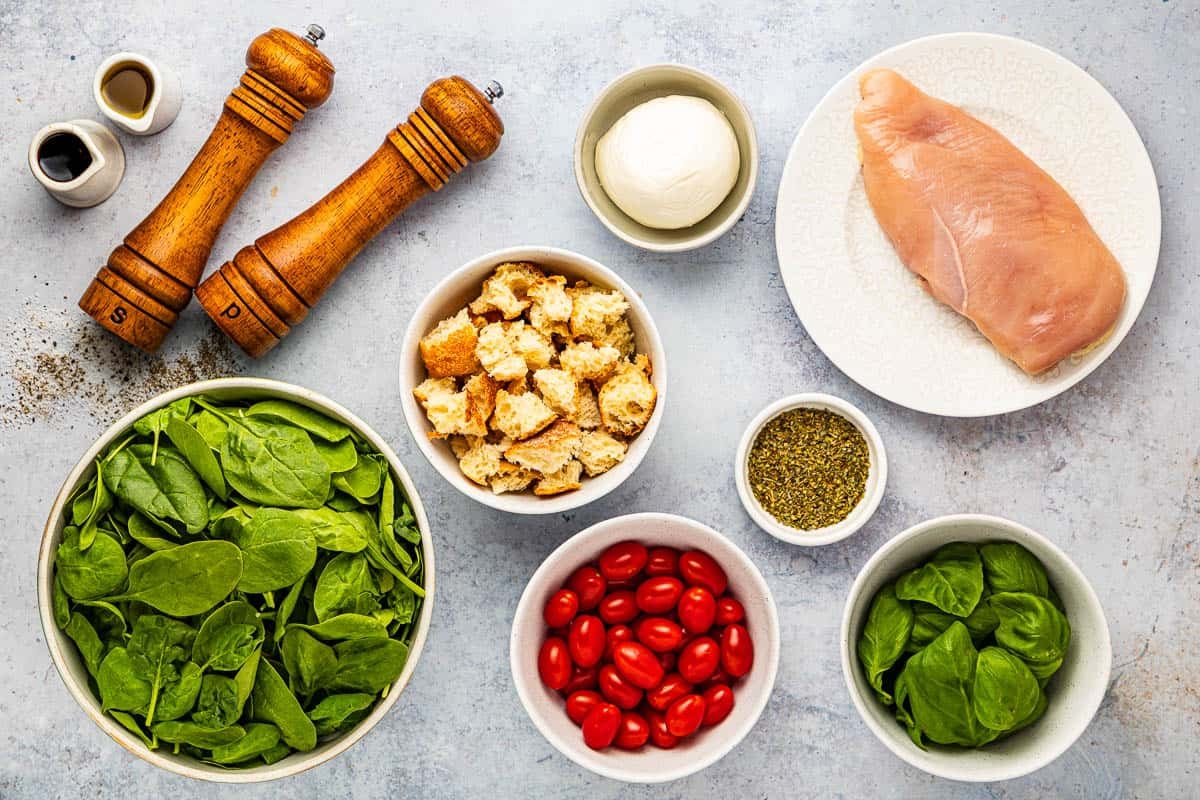 ingredients for chicken caprese salad including chicken breast, olive oil, italian seasoning, salt, pepper, spinach, basil leaves, grape tomatoes, mozzarella, olive oil and balsamic vinaigrette.