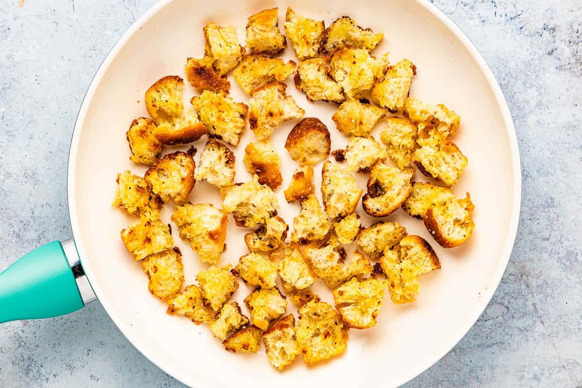 torn pieces of bread being toasted in a skillet to make croutons.