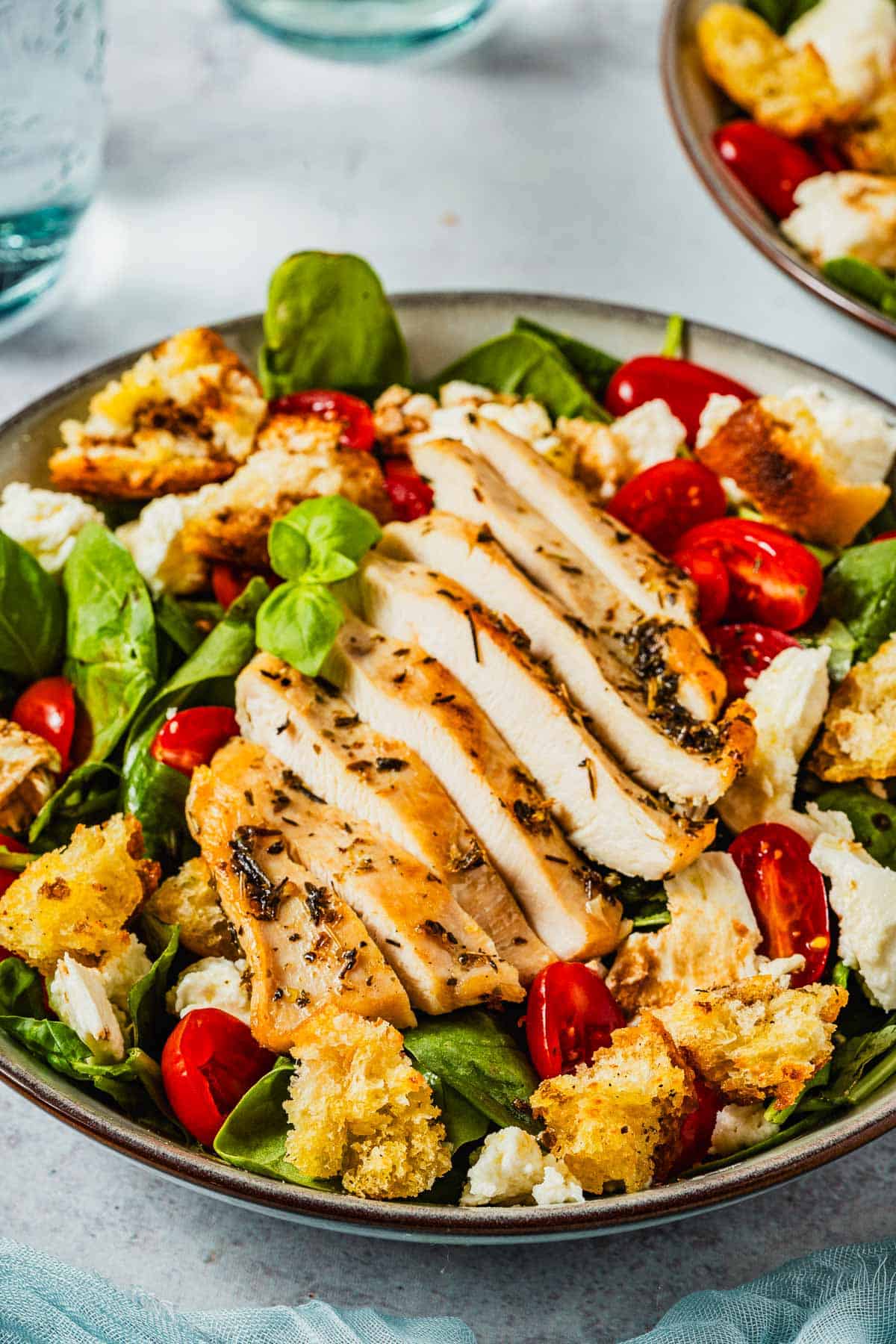 a chicken caprese salad topped with basil, cherry tomatoes, mozzarella cheese and croutons in a bowl.