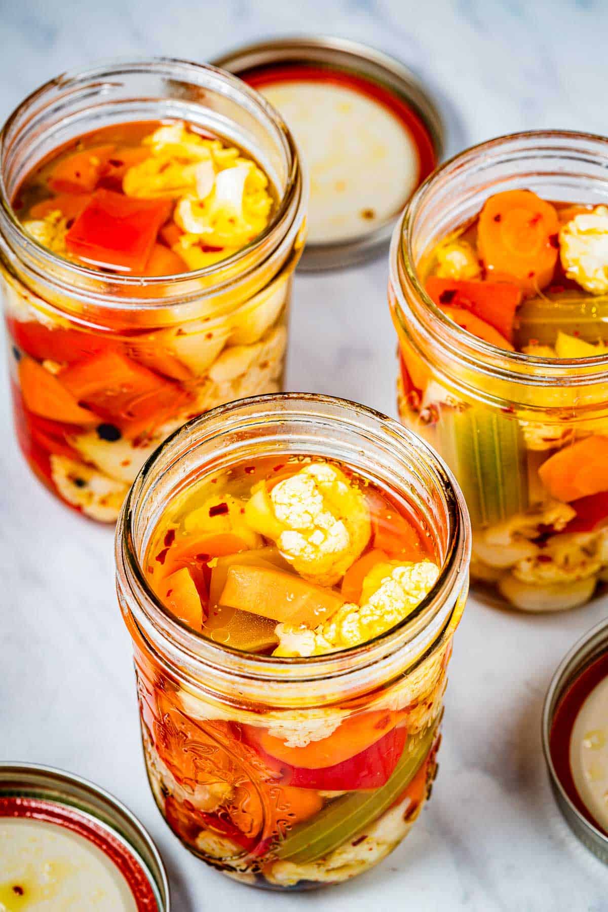 three jars of giardiniera italian pickled vegetables with a lid next to each.