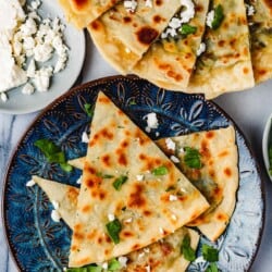 overhead photo of 3 gozleme turkish flatbread triangles on a blue plate and a serving platter with several gozleme triangles next to a plate of crumbled feta.