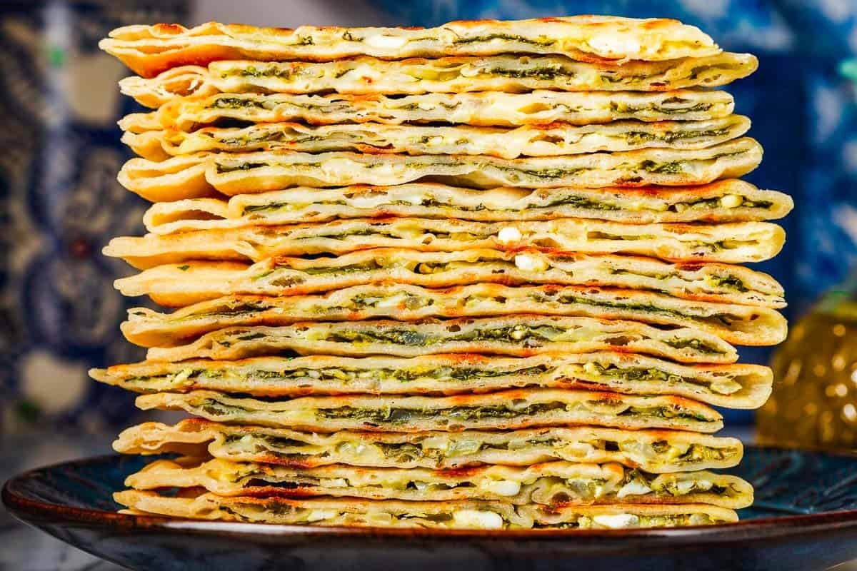 close up of several gozleme turkish flatbread triangles stacked on a blue plate.