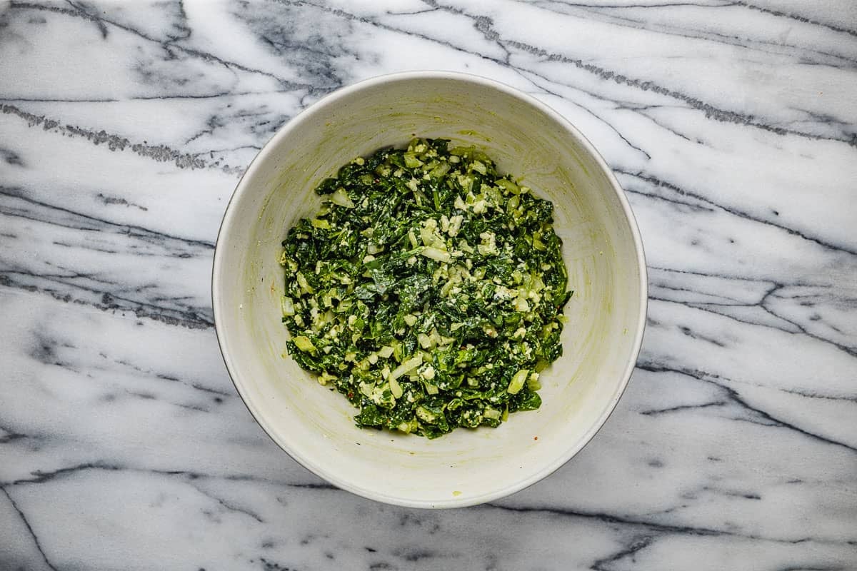 filling for the gozleme including baby spinach, chopped onion, olive oil, salt, pepper and aleppo pepper mixed together in a white bowl.