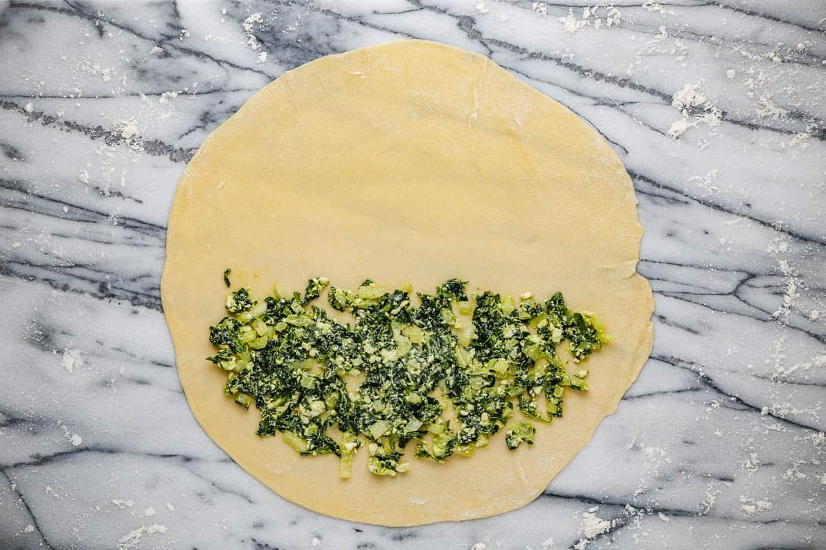 gozleme dough rolled into a circle with the spinach filling covering one half.