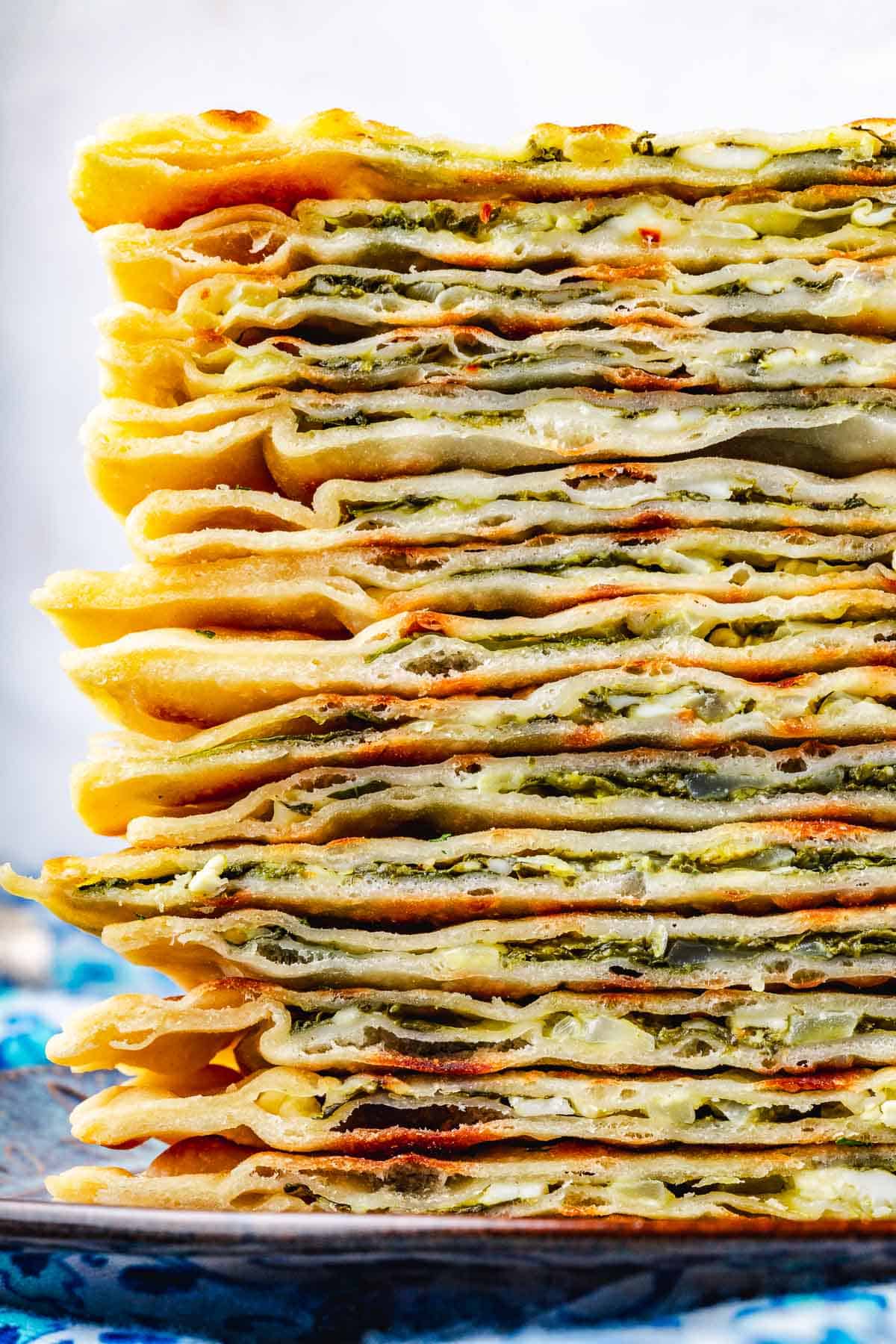 close up of several gozleme turkish flatbread triangles stacked on a blue plate.