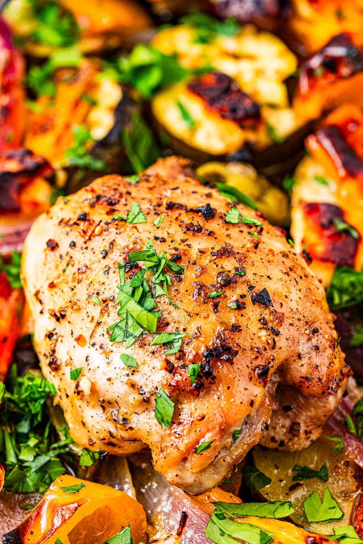 close up of a baked chicken thigh on a bed of roasted vegetables.