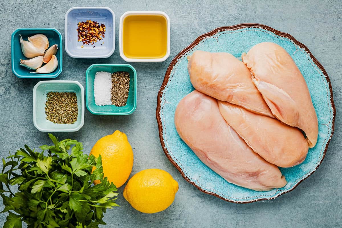 ingredients for lemon garlic chicken including lemons, chicken breast, parsley, olive oil, salt, pepper, italian seasoning, garlic, and red pepper flakes.