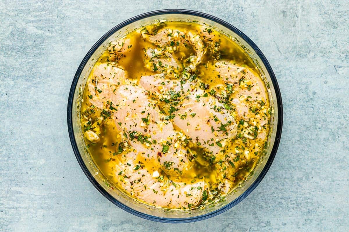 raw chicken breasts marinating in a glass bowl.