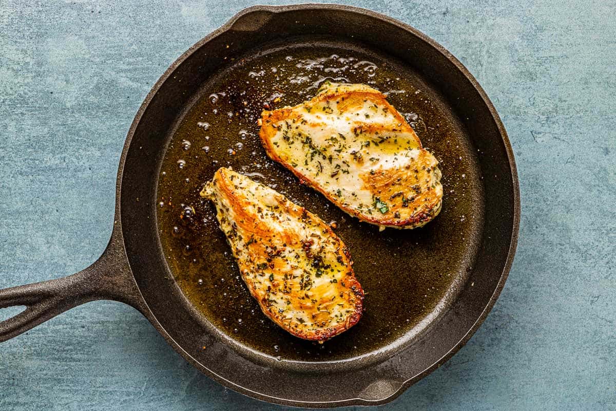 2 pieces of lemon garlic chicken sauteeing in a cast iron skillet.