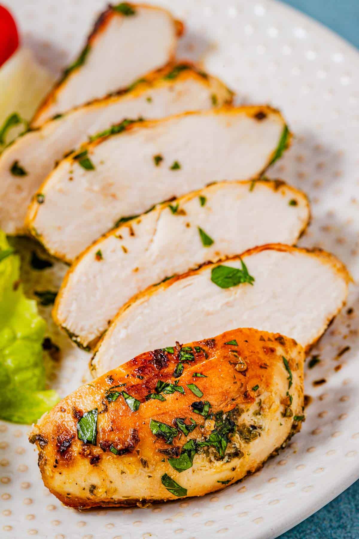 close up of lemon garlic chicken slices on a white plate.