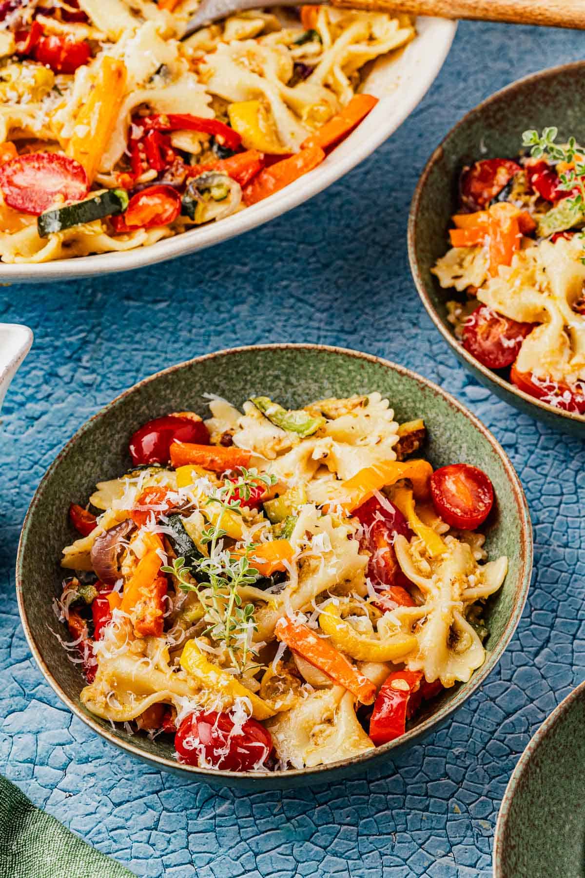 pasta primavera in a green bowl, next to another green bowl and a serving bowl with pasta primavera.