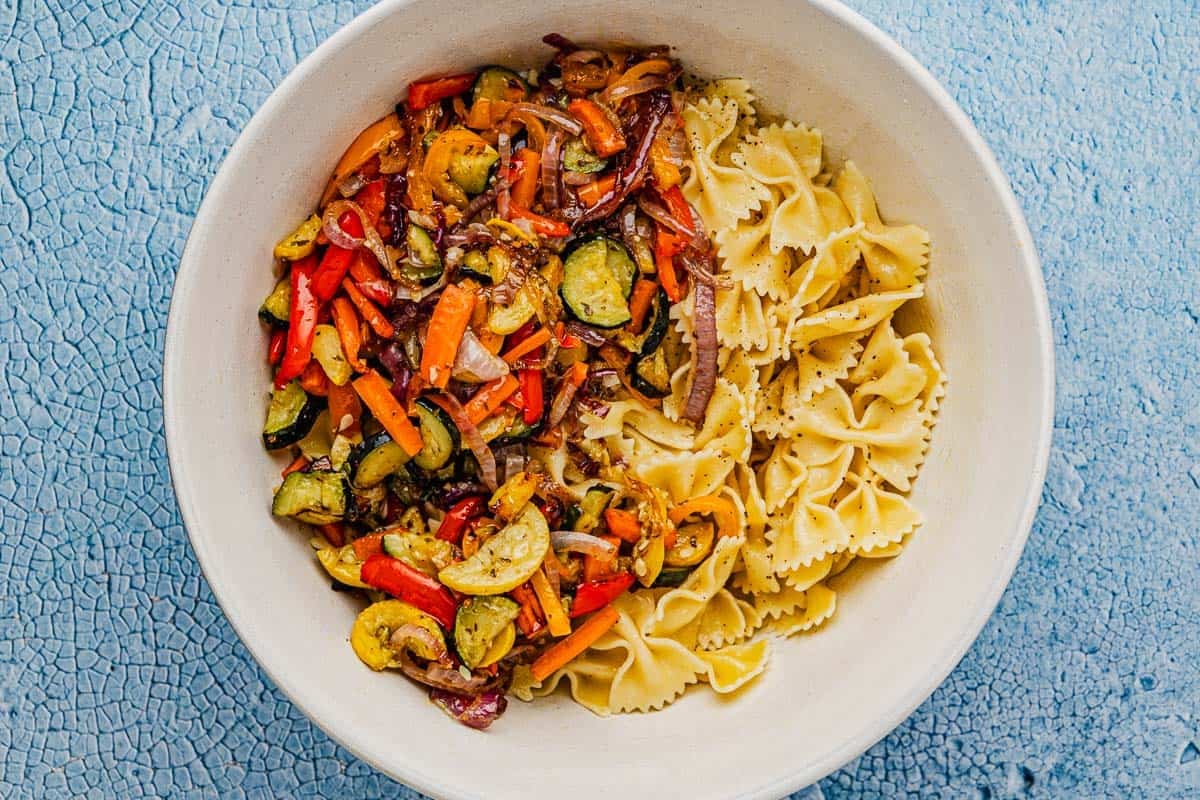 a serving bowl with roasted vegetables and bow tie pasta.