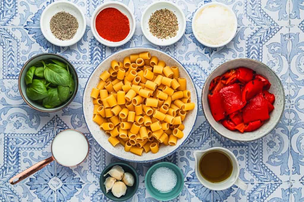 ingredients for roasted red pepper pasta including rigatoni, olive oil, 4 garlic cloves, whole milk, basil, dried oregano, paprika, salt, pepper, and parmesan cheese.