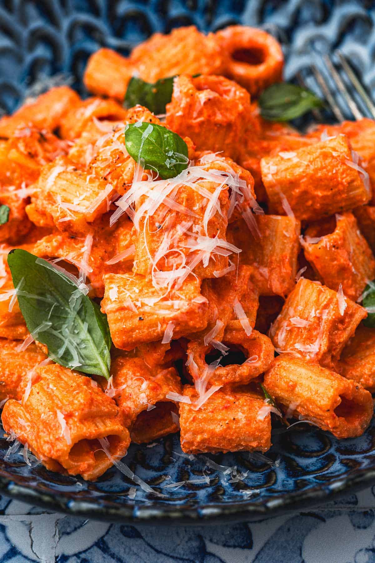 close up of a blue plate with creamy roasted red pepper pasta topped with parmesan cheese and basil.