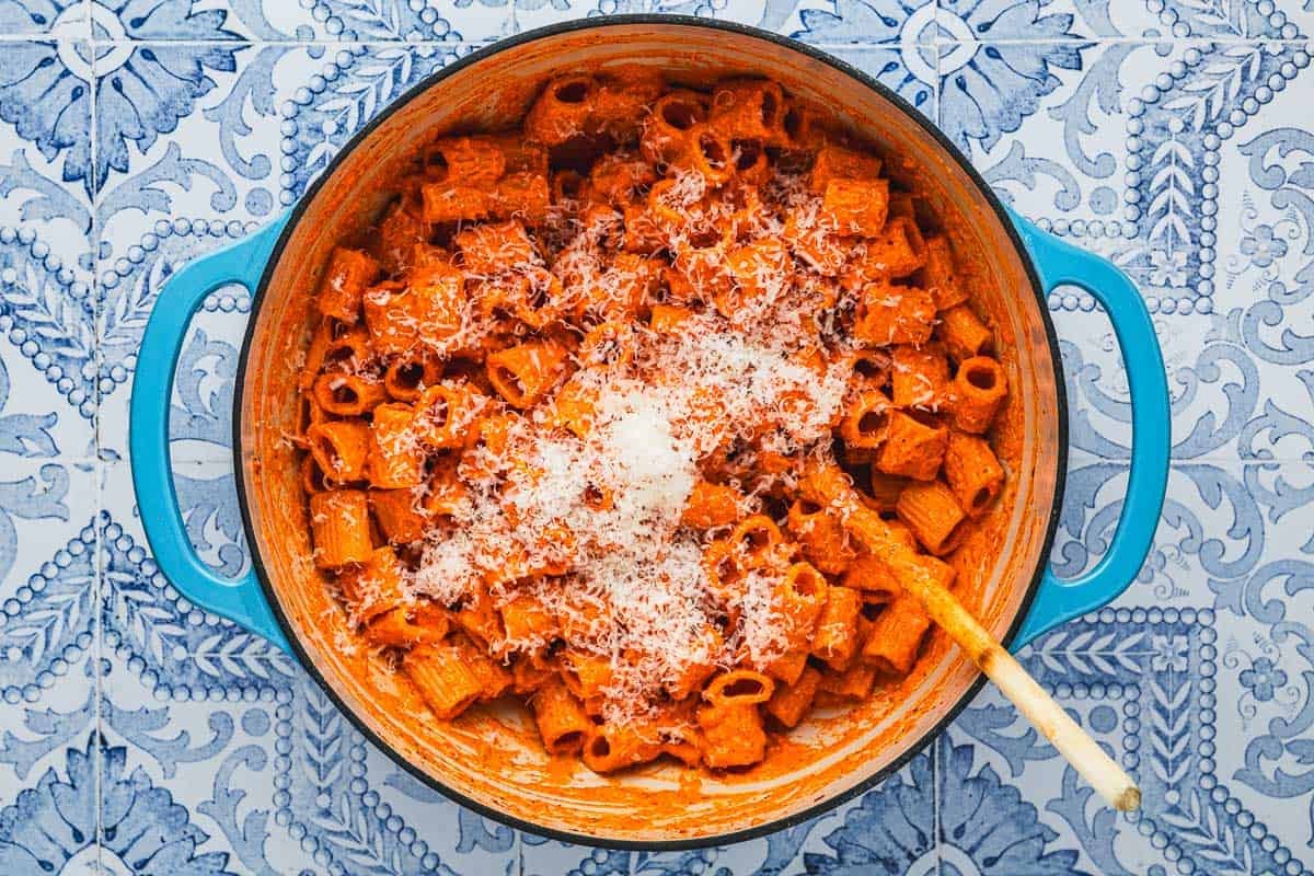 cooked roasted red pepper pasta topped with parmesan cheese in a blue pot with a wooden spoon.