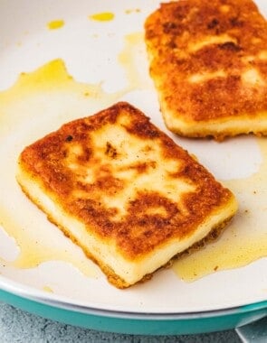 close up of two slices of saganaki fried greek cheese in a skillet.