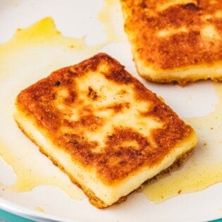 close up of two slices of saganaki fried greek cheese in a skillet.