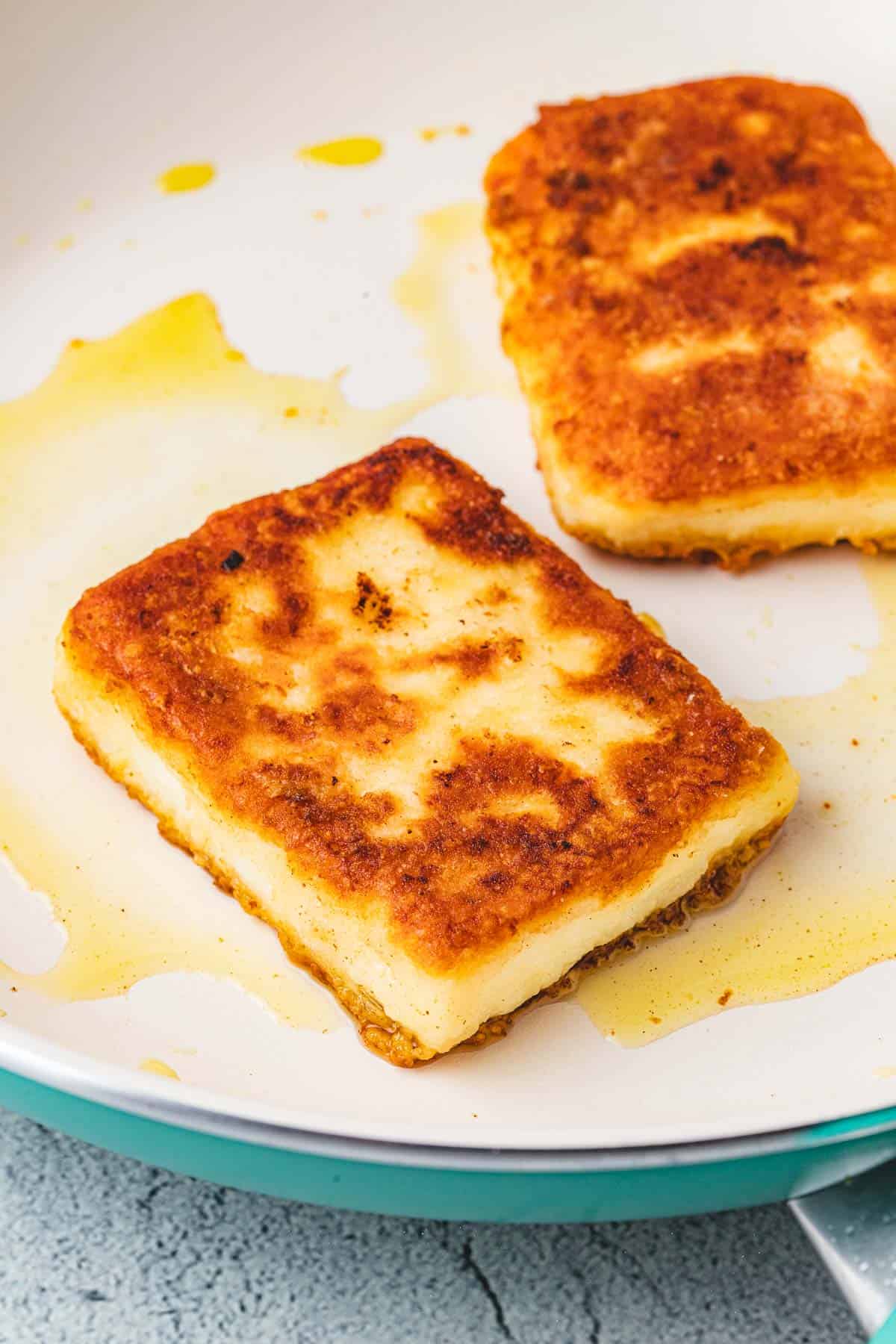 close up of two slices of saganaki fried greek cheese in a skillet.