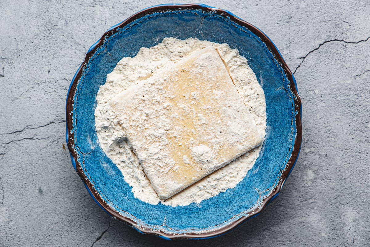 a slice of cheese being coated with flour in a bowl.