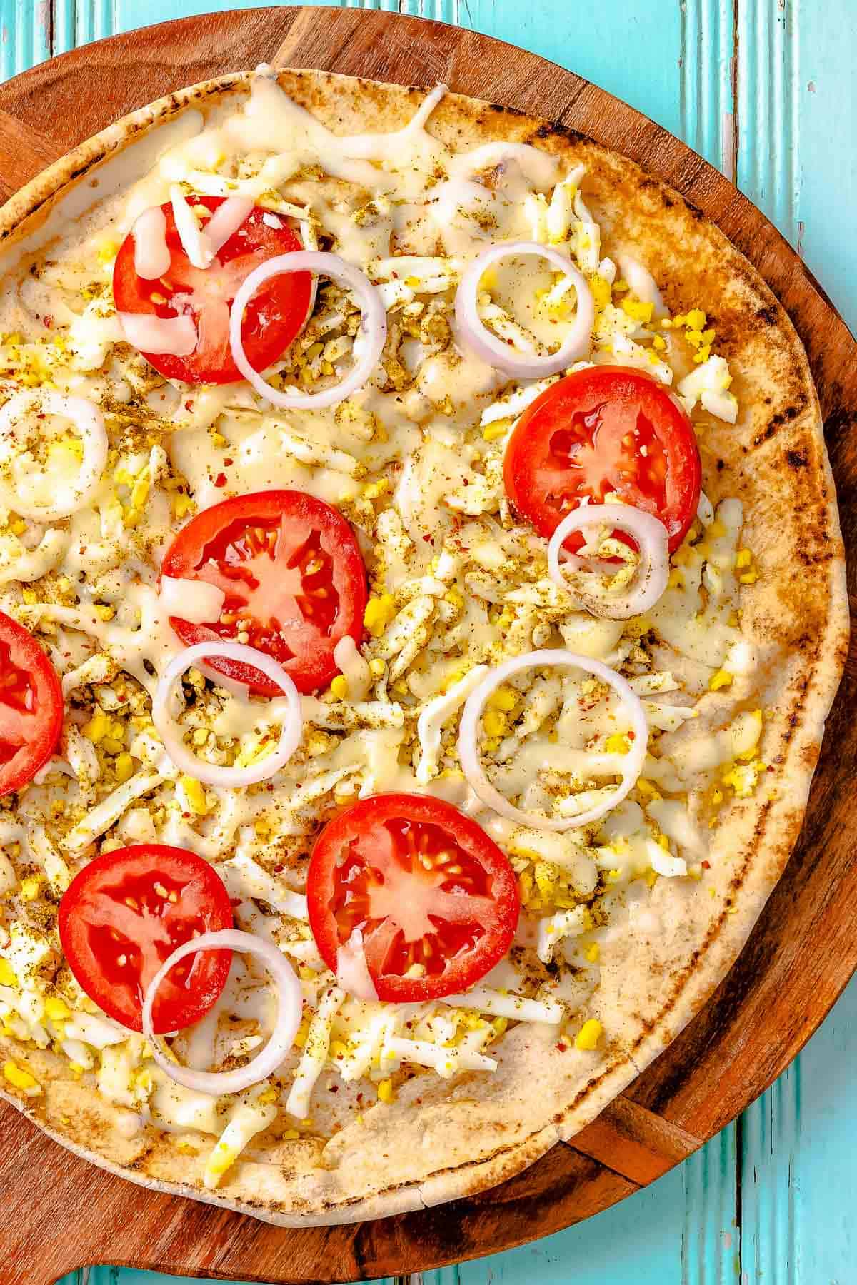 overhead close up photo of a baked pita breakfast pizza on a wooden serving platter.