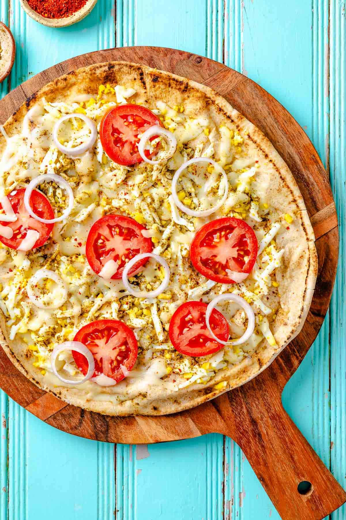 overhead photo of a baked pita breakfast pizza on a wooden serving platter.