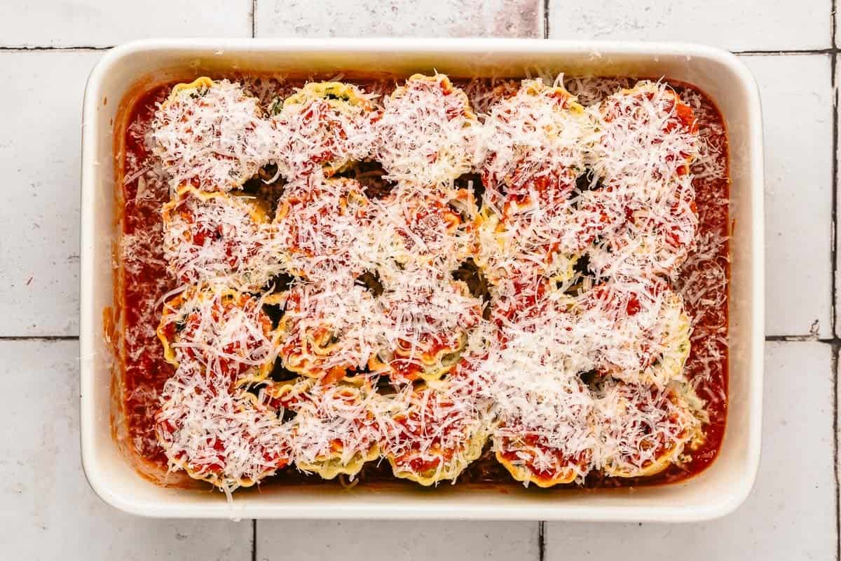 20 unbaked lasagna roll ups in a baking dish with sauce, topped with parmesan cheese.