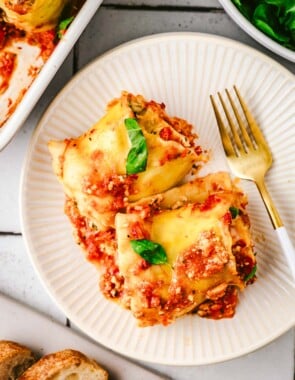 two lasagna roll ups on a white plate with a fork.