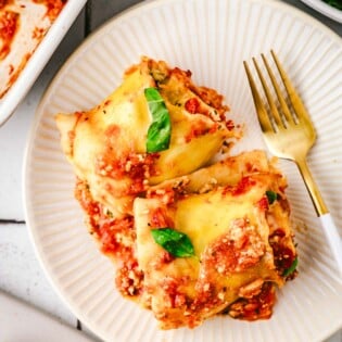 two lasagna roll ups on a white plate with a fork.