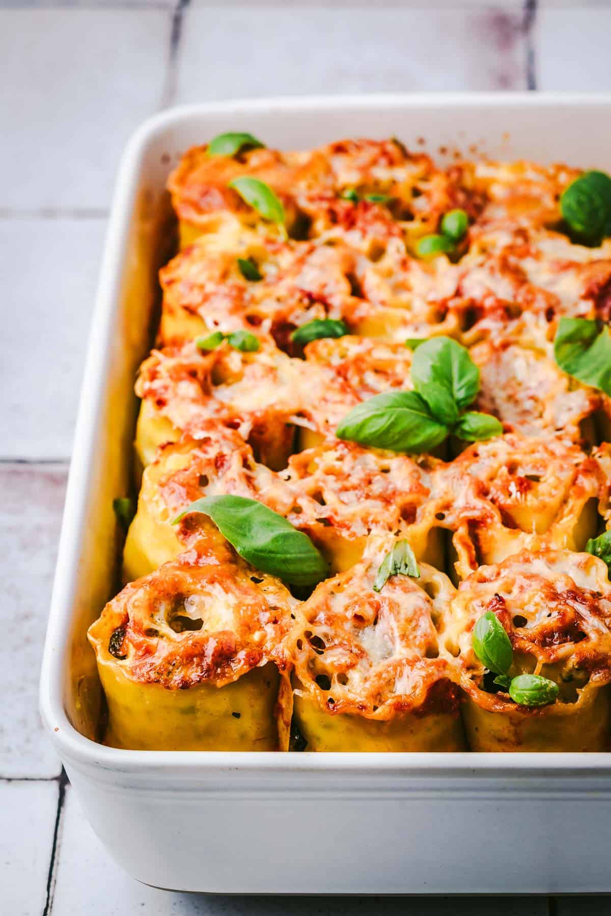 baked lasagna roll ups in a baking dish topped with basil leaves.