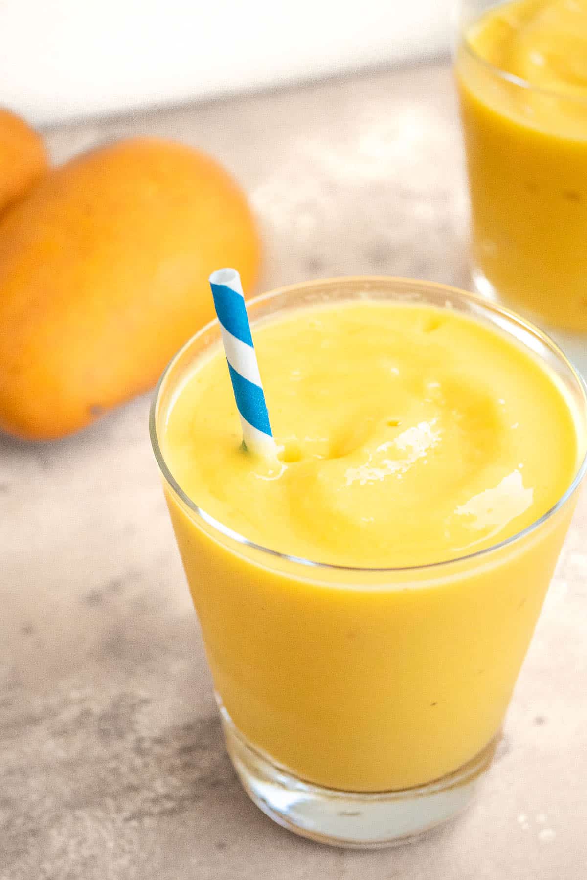 Mango smoothie in a glass with a blue and white striped straw.