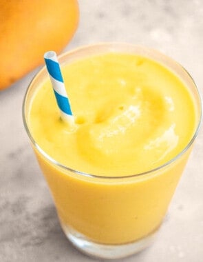 One mango smoothie in a glass with a blue straw.