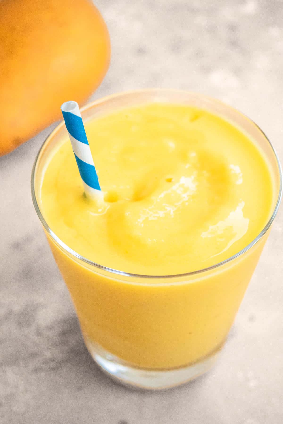 One mango smoothie in a glass with a blue straw.