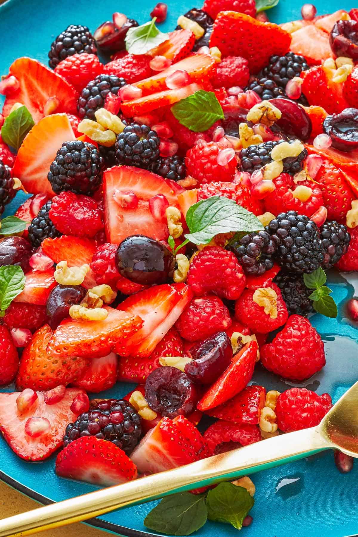 fruit salad topped with mint and walnuts on a blue plate with a gold serving spoon.