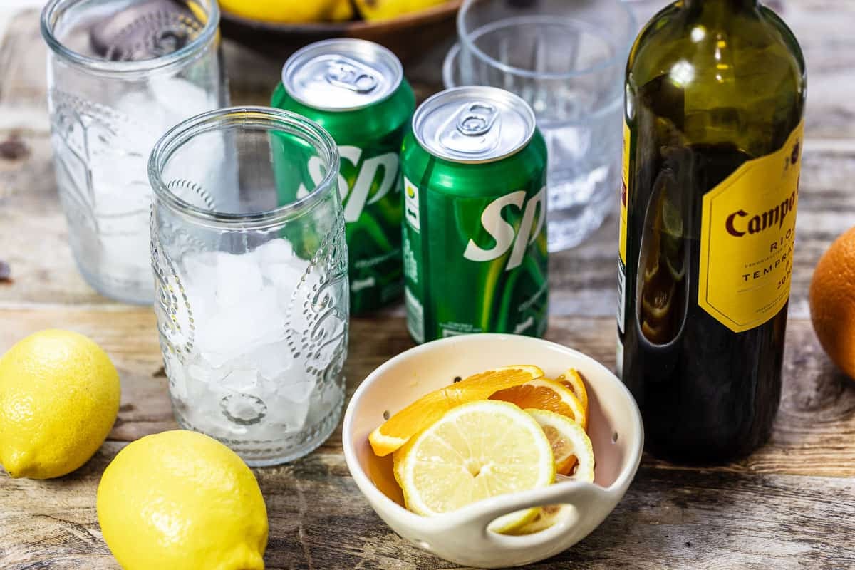 Ingredients for tinto de verano, including lemon and orange slices, sprite, red wine, and ice.