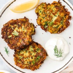 Three zucchini fritters on a plate with a dollop of Greek yogurt and a lemon wedge.