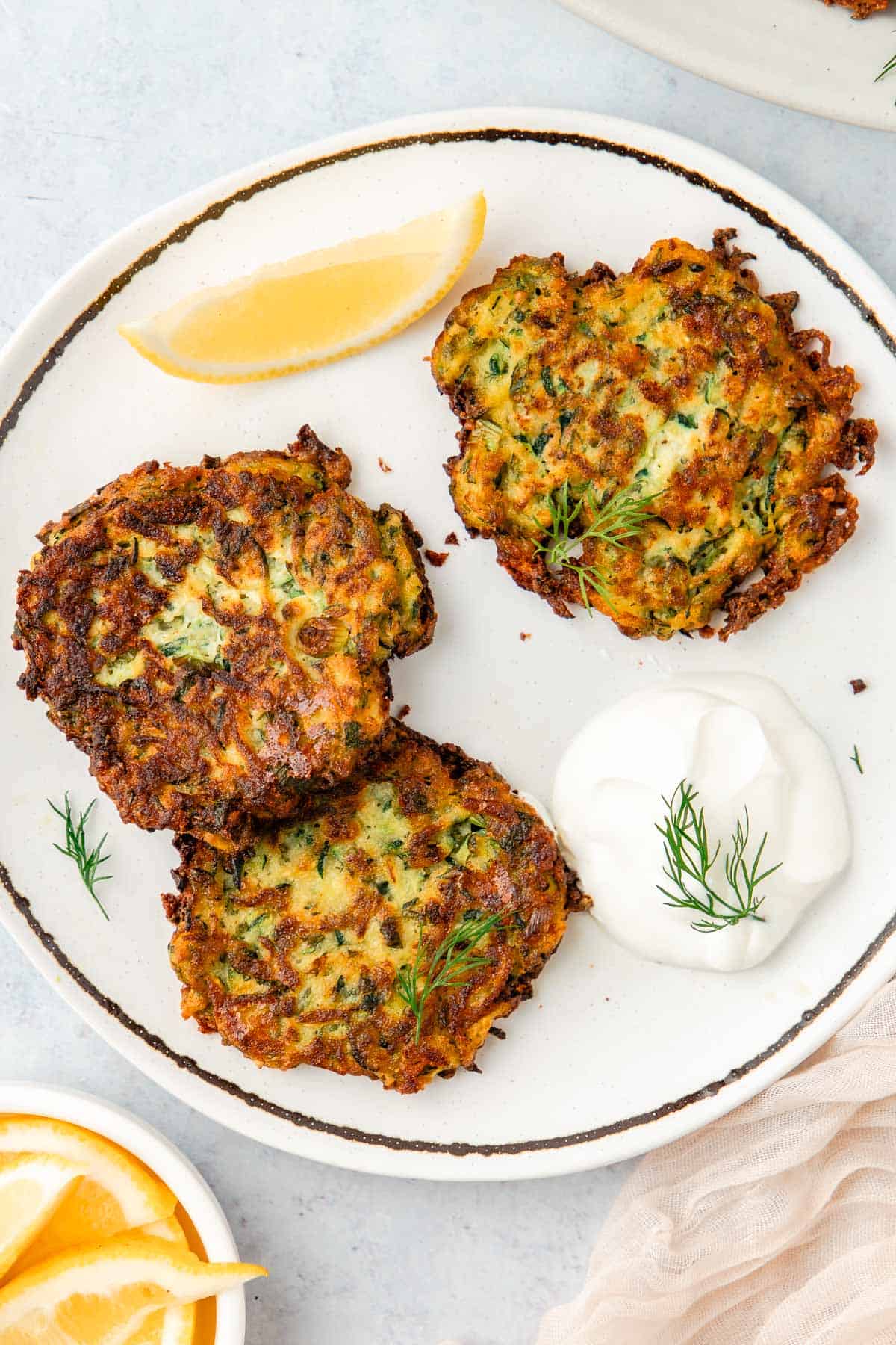 Three zucchini fritters on a plate with a dollop of Greek yogurt and a lemon wedge.