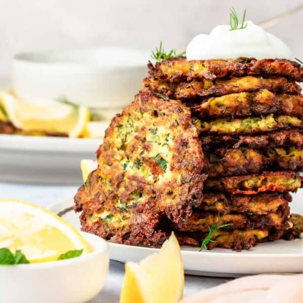 A stack of zucchini fritters with a dollop of Greek yogurt on top and lemon wedges on the side.