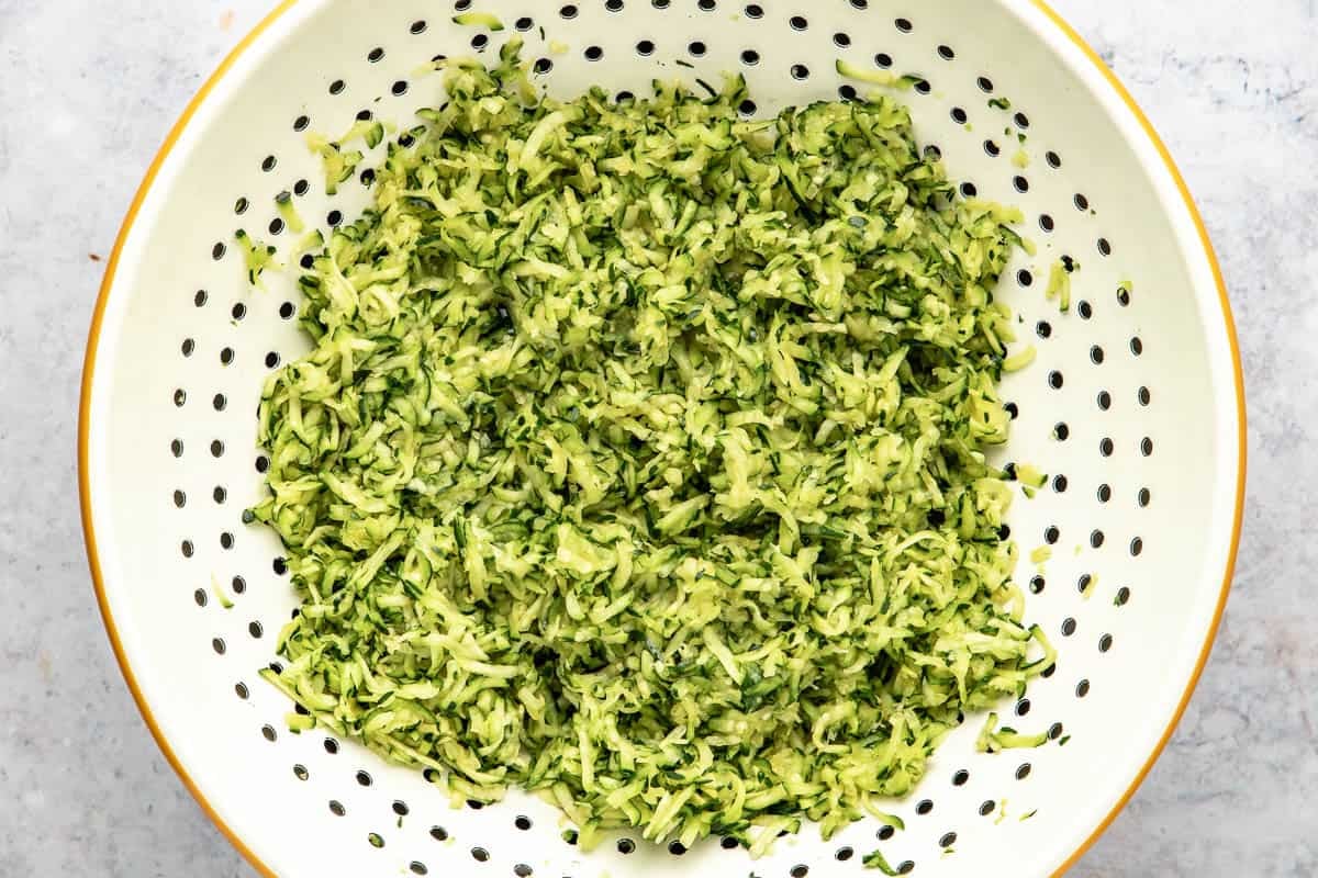 Shredded zucchini draining in a colander.