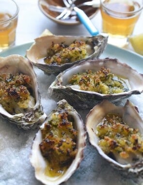 baked oysters with crispy lemon and parsley breadcrumbs on a serving platter with various table setting in the background.