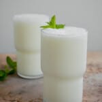 an ayran turkish yogurt drink in a glass garnished with mint leaves, with another glass of ayran in the background.